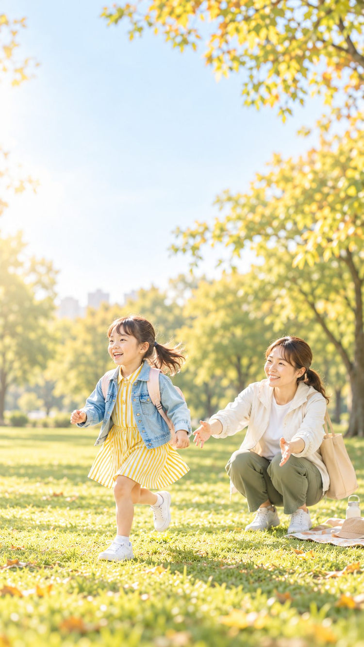 秋の公園で、芝生を駆け出す女の子と、しゃがんで見守るママ