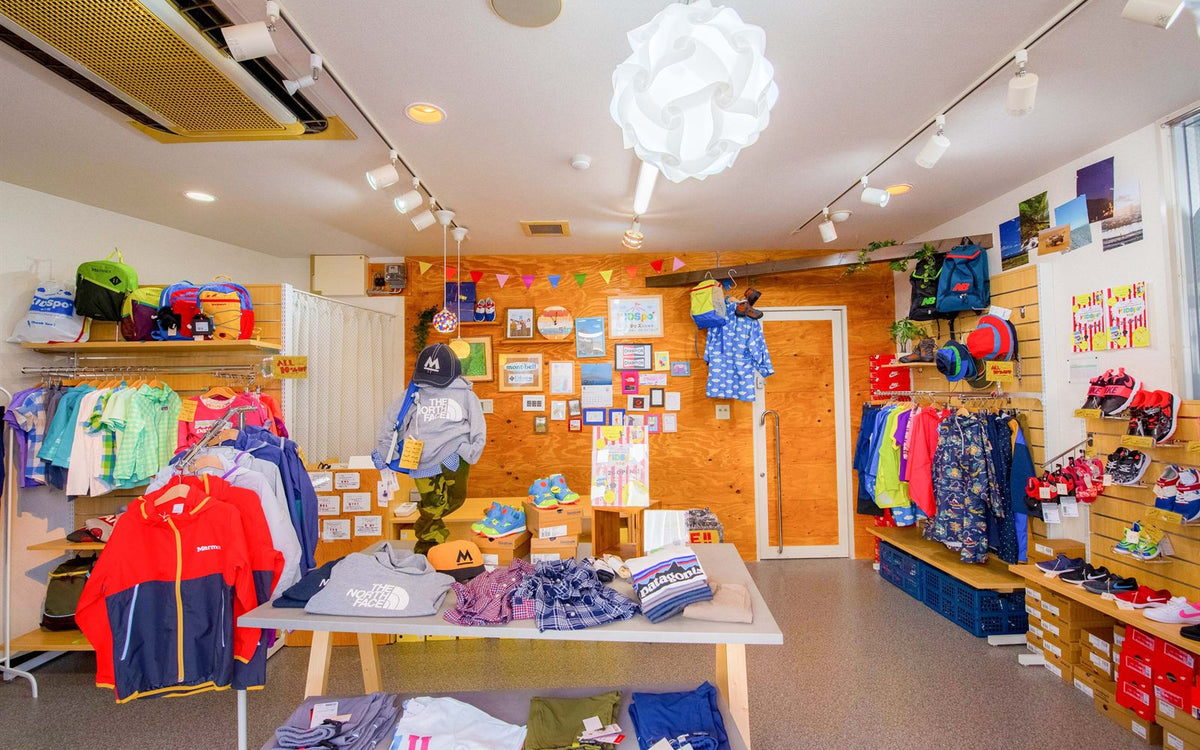 KIDSpo店内。アウトドアブランドのキッズウェアがラックに並び、中央のテーブルにトップスが平置きされている