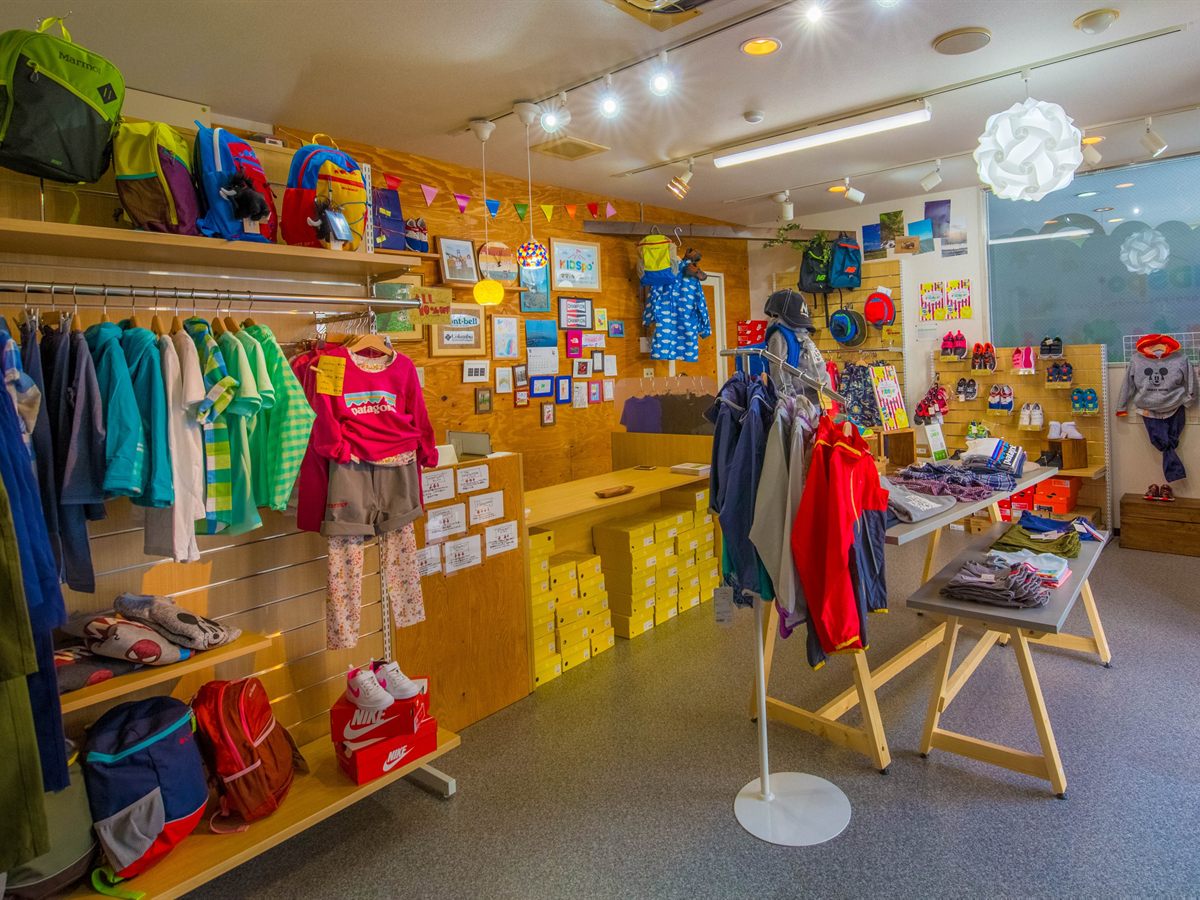 KIDSpo店内のラックに並ぶキッズのアウターとトップス。棚の上にはリュックが並ぶ